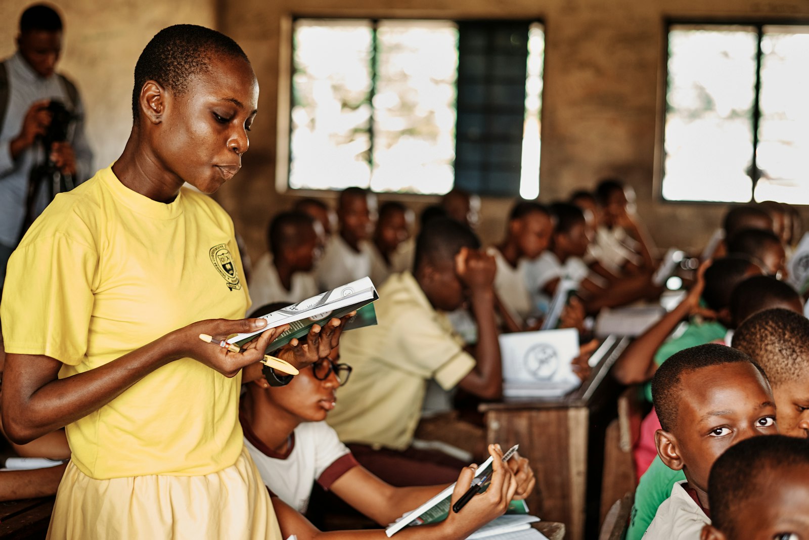 A teacher holding a book while students read in a classroom (illustrative photo)